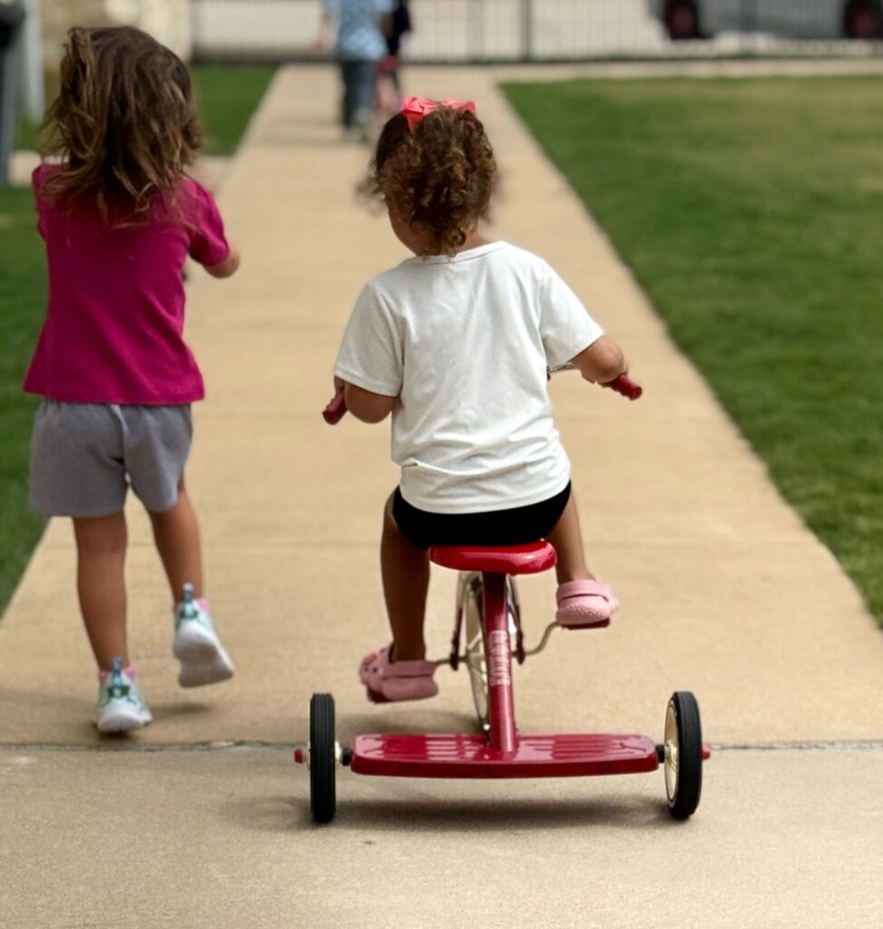 Children riding tricycles up the walkway at Creative Minds